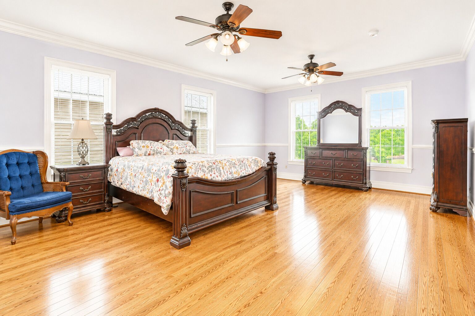 Une chambre à coucher avec un lit en bois, deux tables de chevet, une chaise bleue, une commode et deux ventilateurs de plafond.