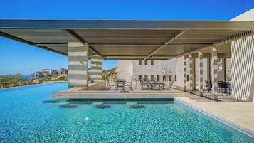 A swimming pool with clear water, outdoor seating, and a view of the ocean.