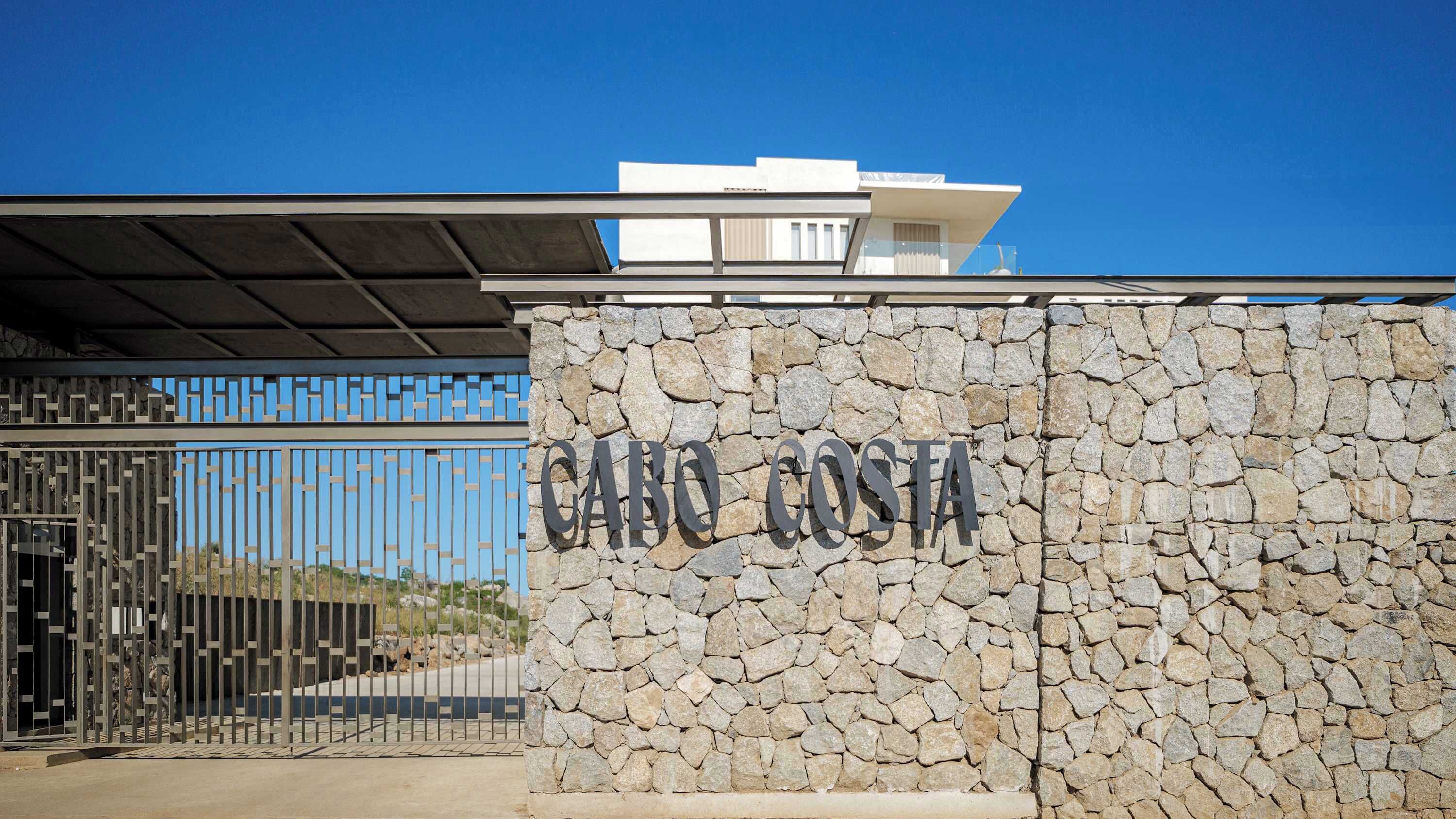 Een stenen muur met de tekst 'CARO COSTA' en een metalen poort.