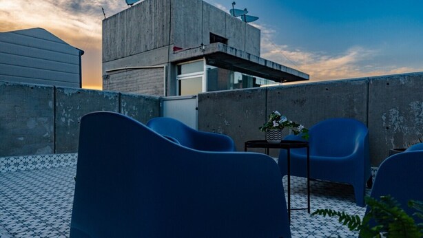 A rooftop terrace with blue chairs, a small table with a potted plant, and a modern building with satellite dishes. - 3BR Roma Norte Penthouse w/ Private Rooftop (Ciudad de México)