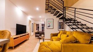 A modern living room with a sofa, a television, and a staircase. - 3BR Roma Norte Penthouse w/ Private Rooftop (Ciudad de México)