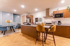 A modern kitchen with a central island, wooden cabinets, a microwave, and a stove. - 3BR Roma Norte Penthouse w/ Private Rooftop (Ciudad de México)