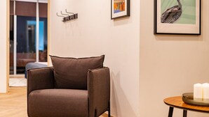 A modern living room with a brown armchair, a small round table with candles, and a framed painting of a bird on the wall. - 3BR Roma Norte Penthouse w/ Private Rooftop (Ciudad de México)