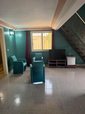 A living room with teal walls, a staircase, and a television on a stand. - Résidence Havre De Paix (La Somone)