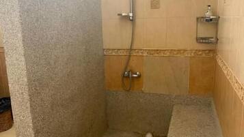 A shower area with a showerhead, a handheld shower, and a small shelf with toiletries.
