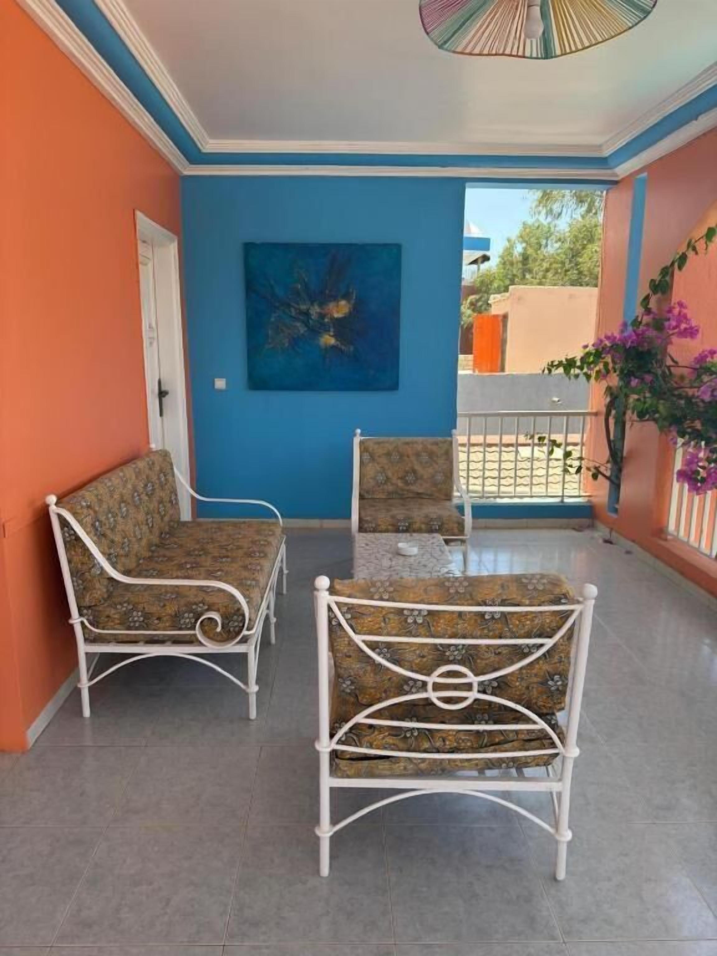 Un balcon avec deux chaises en métal blanc et une table, un mur bleu et une porte.