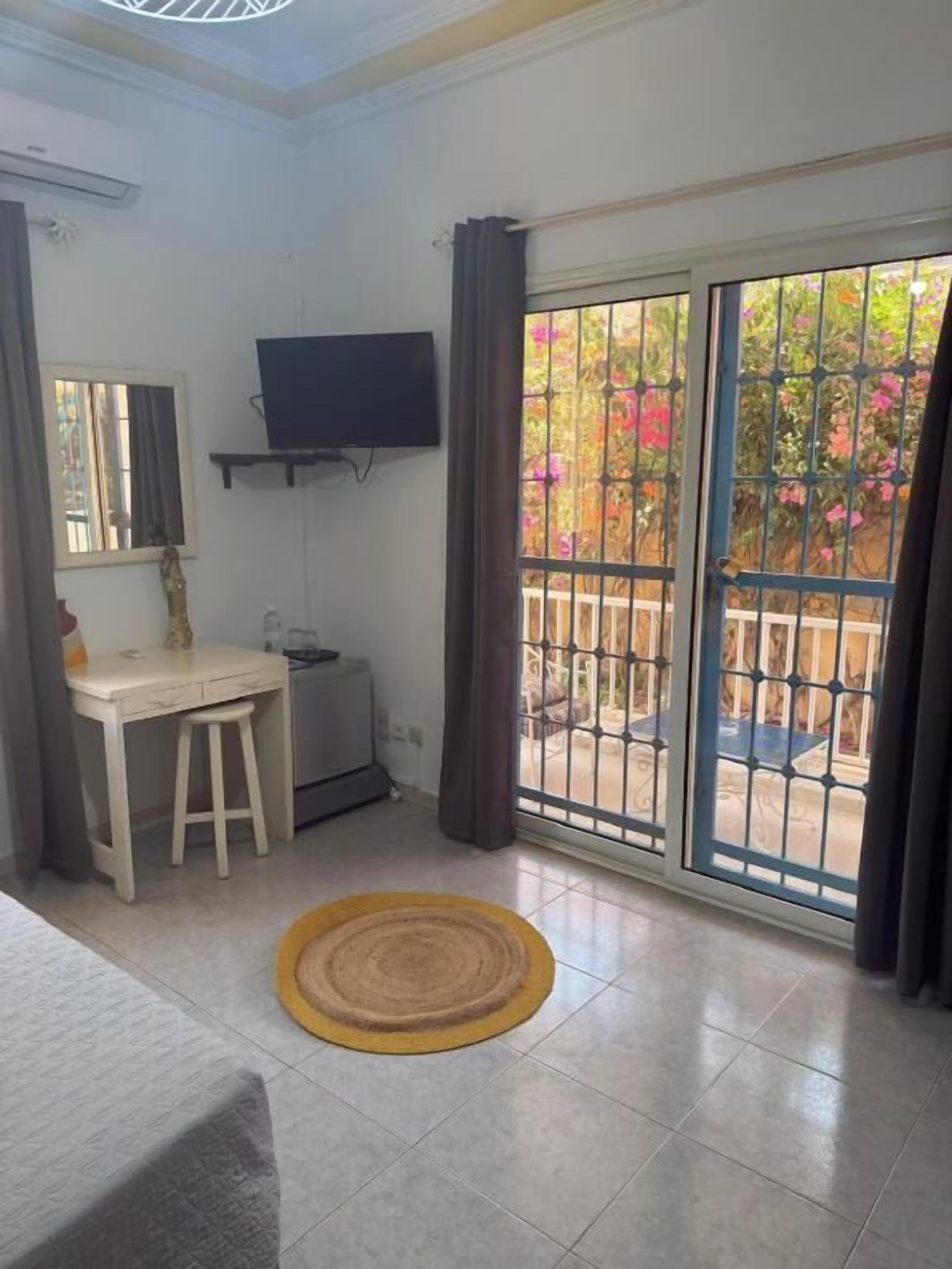 Une chambre comprenant un lit, un bureau, une chaise, un téléviseur et une porte-fenêtre coulissante donnant sur un espace extérieur avec vue sur un jardin.