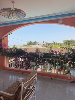 Un balcón con vista al mar, barandilla decorada con flores y una banca.
