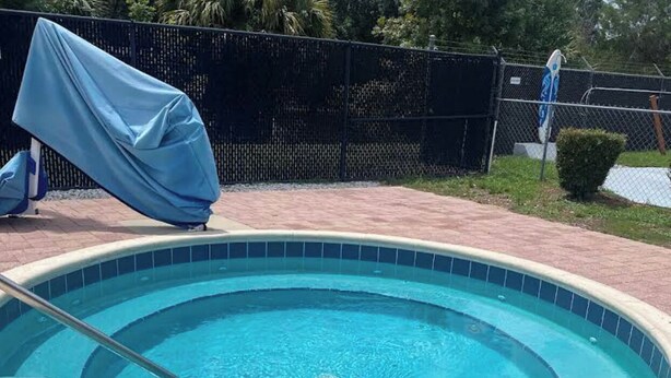 A swimming pool with a tiled edge, a metal ladder, and a covered chair.