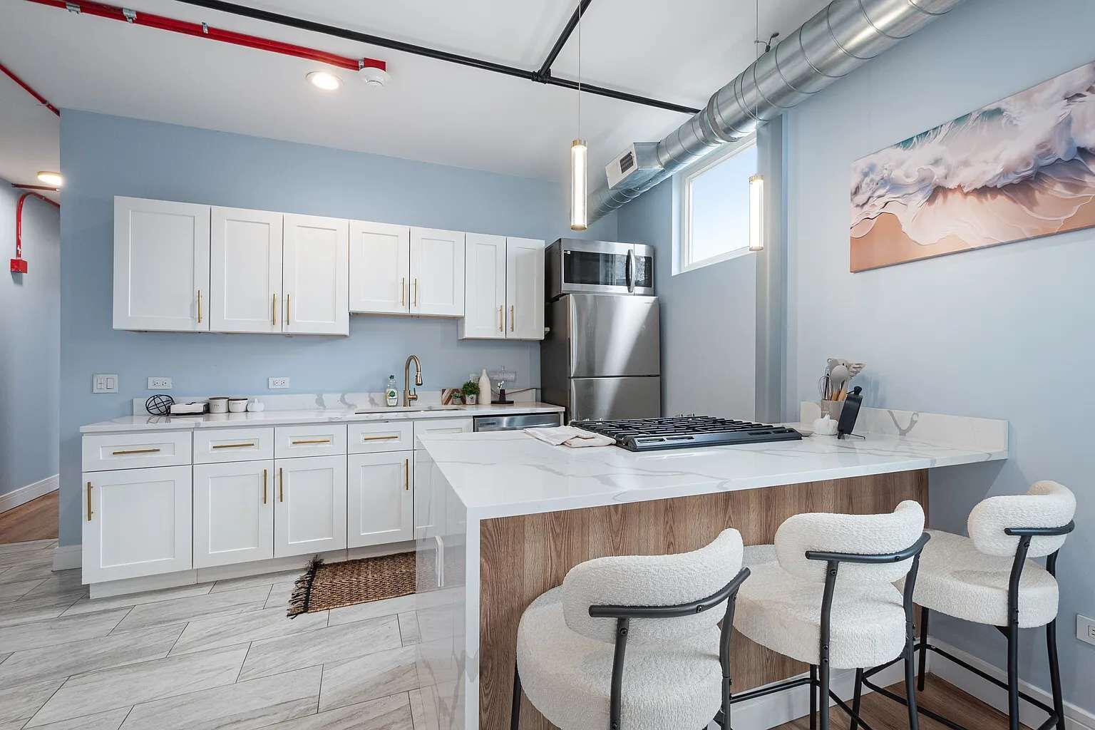Une cuisine moderne avec des meubles blancs, un îlot central doté de tabourets de bar, des appareils en acier inoxydable et une grande fenêtre.