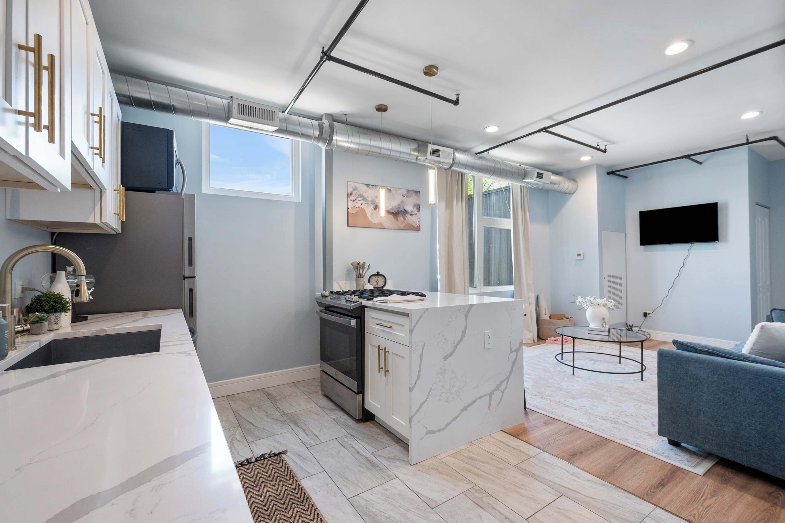 Uma cozinha moderna com uma ilha central, uma área de refeições com um sofá azul, e uma televisão de tela plana na parede.