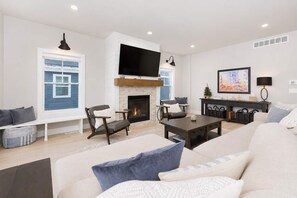 A modern living room with a fireplace, comfortable seating, a flat-screen TV, and a large window with a view. - Blue Haven | 5 min walk to beach • pool • grill (South Haven)