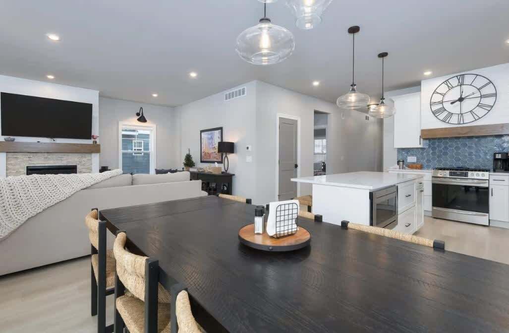 A modern kitchen with a central island, a dining area with a dark wood table, and a living space with a sofa and a TV.