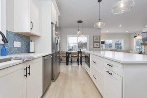 A modern kitchen with white cabinetry, a central island, and pendant lighting. - Blue Haven | 5 min walk to beach • pool • grill (South Haven)