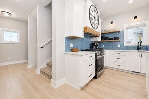 A modern kitchen with white cabinetry, a built-in stove, and a blue tiled backsplash. - Haven House | 5 min walk to beach • pool • grill (South Haven)