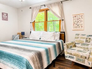 Ein Schlafzimmer mit Bett, Stuhl, Fenster und einem Wandbild.