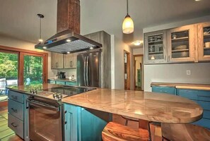 A modern kitchen with a central island, stainless steel appliances, and blue cabinetry. - Wildhaus Retreat | Hot Tub • Private Walking Trail (South Haven)