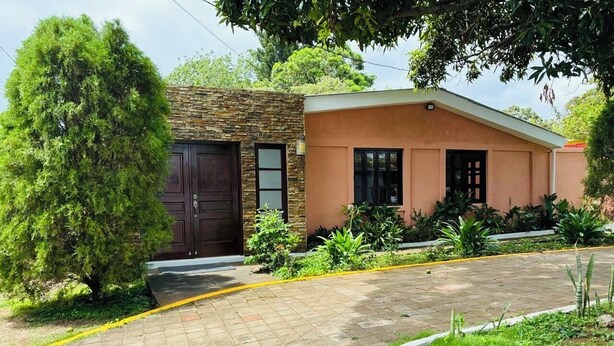 A residential property with a stone facade, a paved driveway, and a well-maintained lawn. - Charming 4-bedroom house in Managua perfect for your getaway near everything ! (Managua)