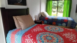 Een kamer met een bed, nachtkastje, lamp en raam met groene gordijnen.