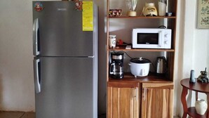 Een kleine keuken met een koelkast van roestvrij staal, een magnetron en houten kastjes.