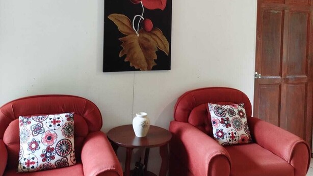 Een kamer met twee rode fauteuils, een kleine ronde tafel en een aan de muur hangend schilderij van een rode bloem.
