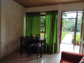 Une pièce comprenant une table à manger et des chaises, un rideau vert et une porte-fenêtre coulissante donnant sur un espace extérieur.