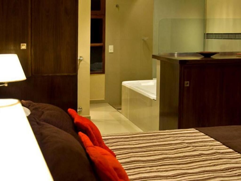 Een hotelkamer met een bed, nachtkastje, lamp, en een badkamer met toilet en douche.