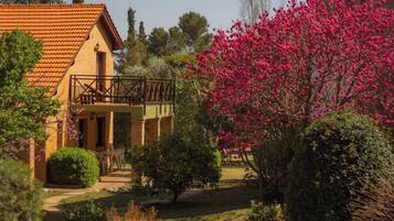 Una casa con balcón, rodeada de un jardín con arbustos y un árbol en flor.