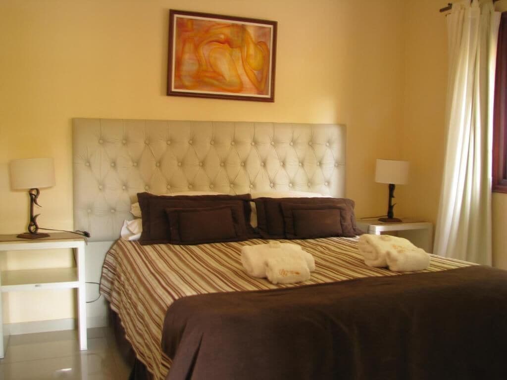 Una camera d'hotel con una testiera imbottita, una coperta a righe, due lampade sui comodini e un quadro appeso al muro.