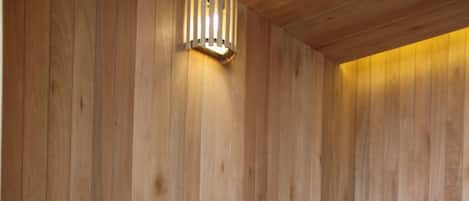 Una sauna de madera con bancos y una mesa, con techo inclinado y una lámpara fijada a la pared.