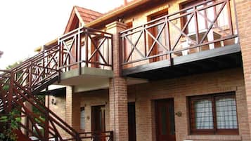 A multi-story building with a brick facade, a metal staircase, and a balcony with white plastic chairs.