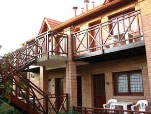 A multi-story building with a brick facade, a metal staircase, and a balcony with white plastic chairs. - Complejo Don Gregorio SPA (Merlo)