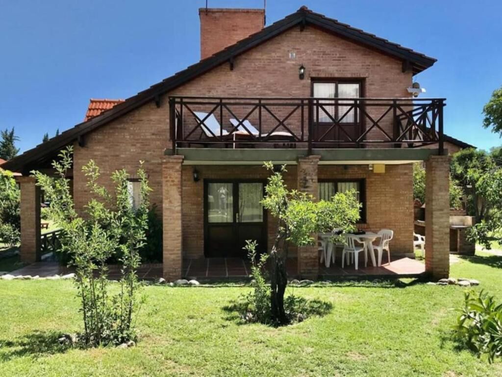 A two-story brick house with a balcony, a covered patio, and a lawn.