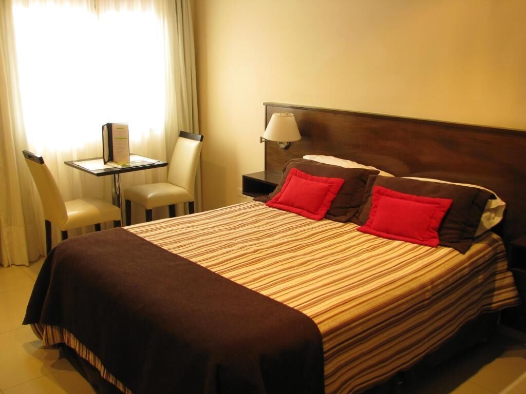 A hotel room with a bed, a nightstand, a lamp, a chair, and a table.