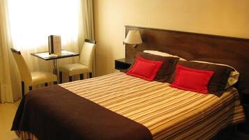 A hotel room with a bed, a nightstand, a lamp, a chair, and a table.