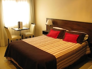 A hotel room with a bed, a nightstand, a lamp, a chair, and a table.