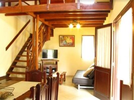 Una habitación con una escalera de madera, un sofá, un televisor y un cuadro en la pared.