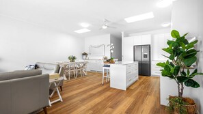 Eine moderne Küche mit weißen Schränken, einem integrierten Kühlschrank und einem Essbereich mit einem weißen Tisch und Stühlen.
