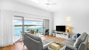 A modern living room with a large sliding glass door to a balcony, a flat-screen TV, and a cozy seating area. - The Anchorage 7 Noosaville (Noosaville)