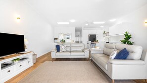 Ein modernes Wohnzimmer mit Flachbildfernseher, zwei Sofas, einem Couchtisch und einer Küche im Hintergrund.
