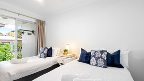 A hotel room with two beds, a nightstand, a lamp, and a view of greenery outside. - The Anchorage 7 Noosaville (Noosaville)
