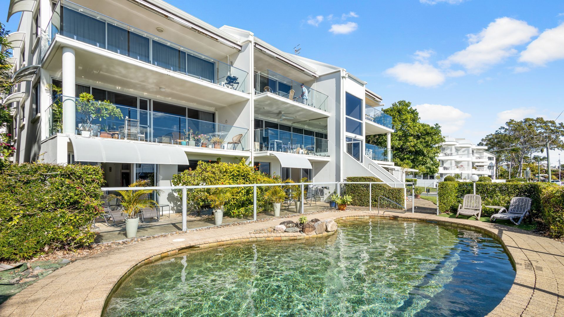 A modern multi-story building with a swimming pool in front.