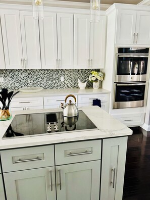 A modern kitchen with white cabinetry, a black stovetop, and stainless steel appliances. - All Ensuites Retreat near Lake & Airport – Pool (Lewisville)