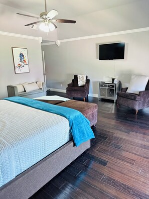 Ein Hotelzimmer mit Bett, Sessel, Fernseher und Deckenventilator.