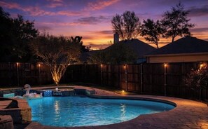 Ein Schwimmbad mit Whirlpool, umgeben von einem Holzzaun, mit Sonnenuntergang im Hintergrund.