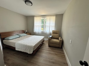 A bedroom with a bed, a chair, a nightstand, and a window with curtains. - Lake House, Boating, Kayaking, Huge backyard (Hartwell)