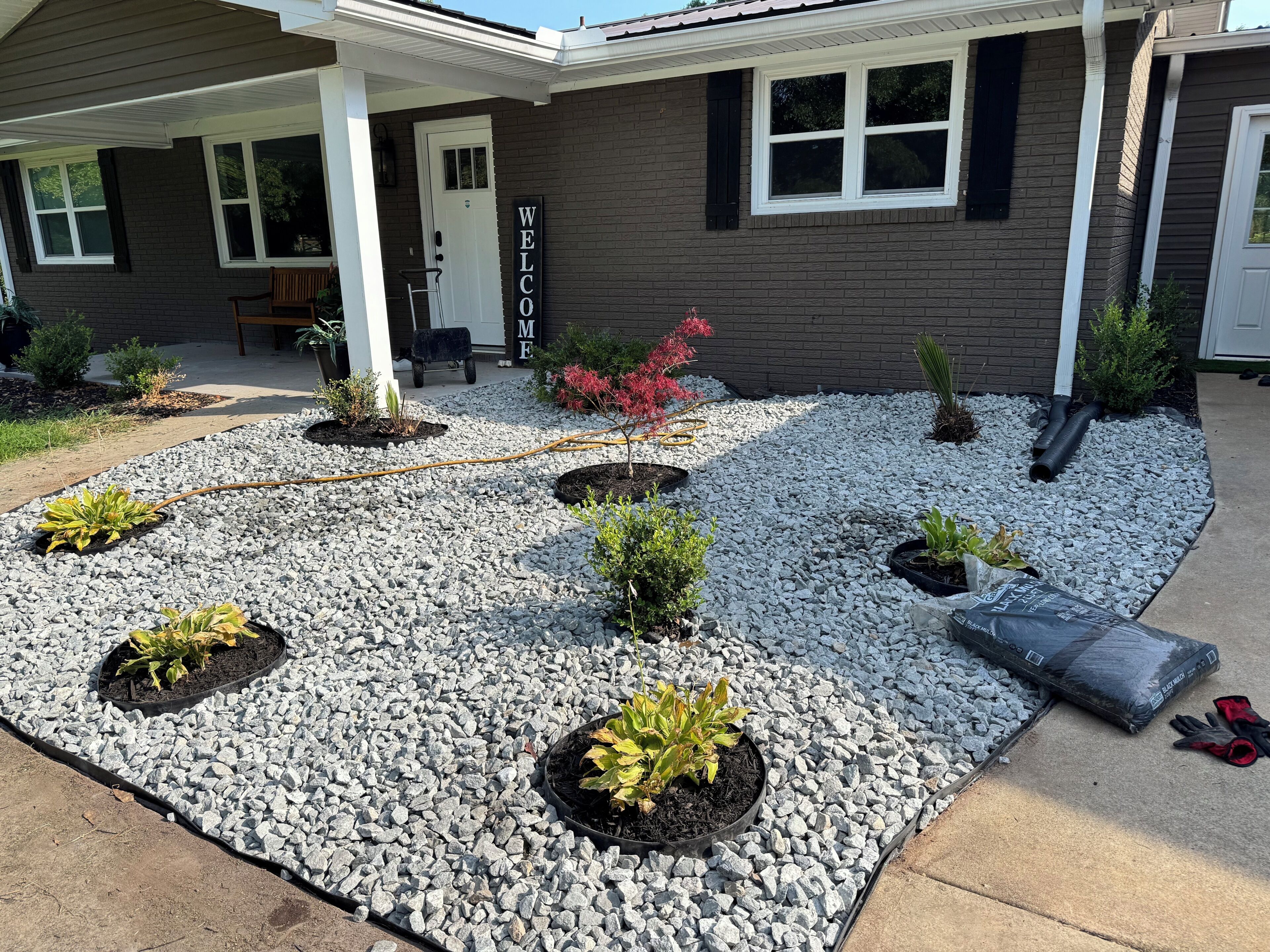 A residential house with a gravel driveway, a welcome sign, and potted plants.