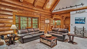 A log cabin interior with a sectional sofa, a coffee table, and a dining area.