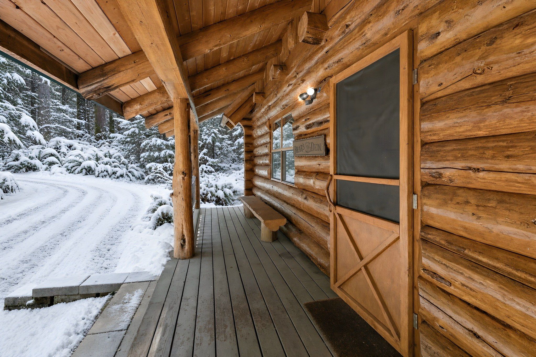 A wooden cabin with a covered porch and a snow-covered landscape.