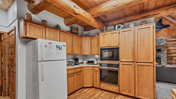 A kitchen with wooden cabinets, a refrigerator, a microwave, and a stone fireplace.